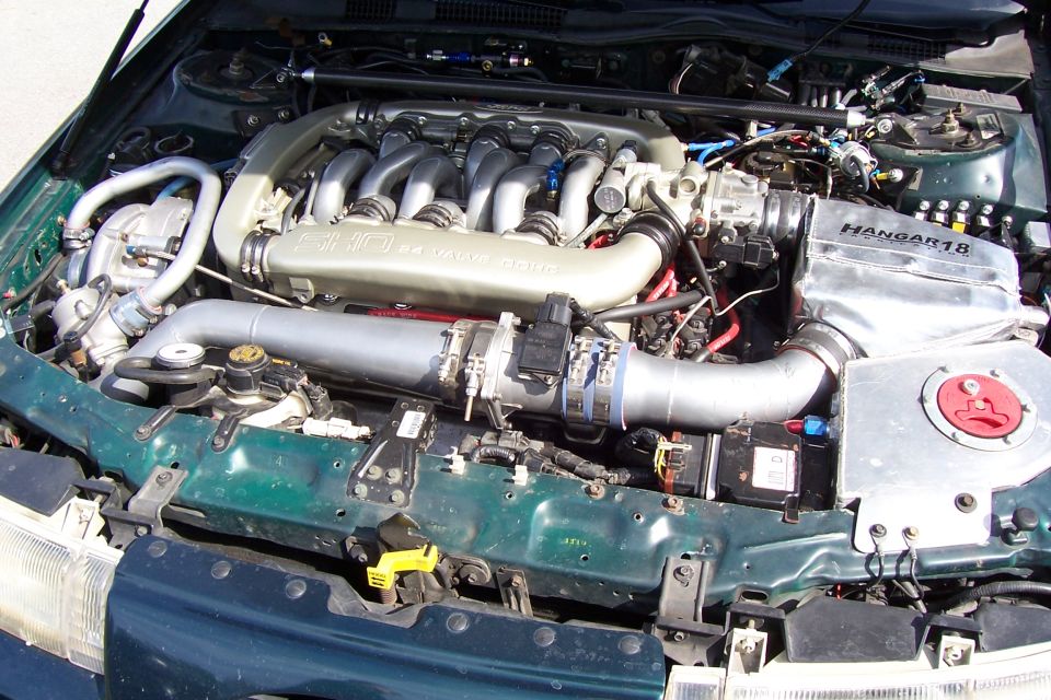 Green engine bay with V6 engine, silver intake pipes, and "Hangar18" label on a silver cover