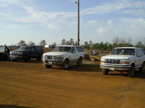 1996 Ford Bronco - Three Ford Broncos are parked on a dirt lot under a bright blue sky.