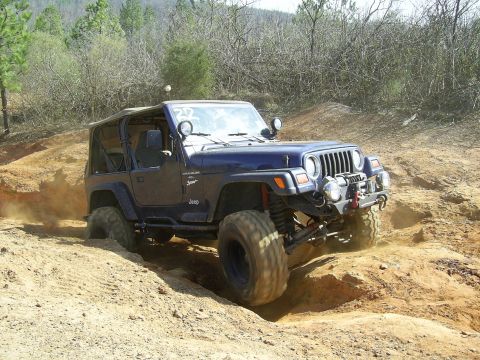 1996 Ford Bronco - Jeep Wrangler TJ model tackling a challenging off-road course with dust kicking up.