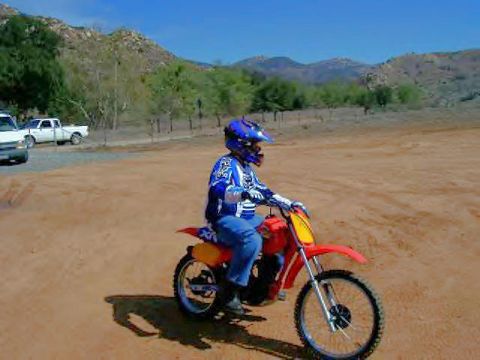 2002 Ford Crown Victoria - A rider on a red dirt bike navigates a dusty track with mountains in the background.