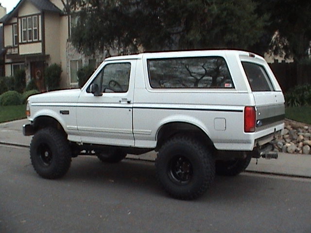 Lifted white Ford Bronco on black wheels parked on a suburban street