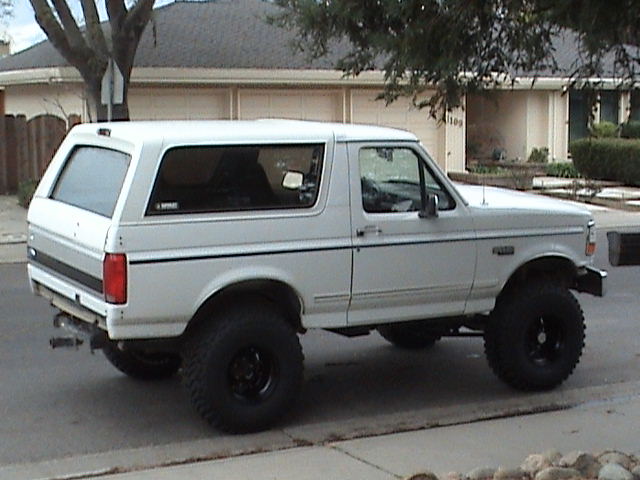 Lifted white Ford Bronco parked at a suburban curb, rear three-quarter view