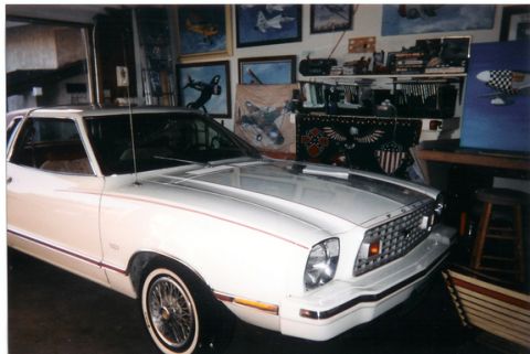 1978 Ford Mustang II - A white 1978 Ford Mustang II is parked indoors, surrounded by various paintings and memorabilia.
