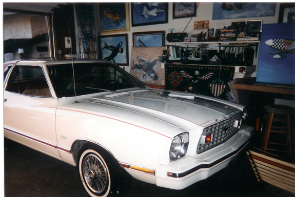 White 1978 Ford Mustang II coupe parked in a garage with artwork on the walls