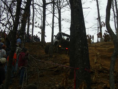 1996 Ford Bronco - An off-road SUV navigates a challenging incline during an event, observed by a crowd of onlookers.