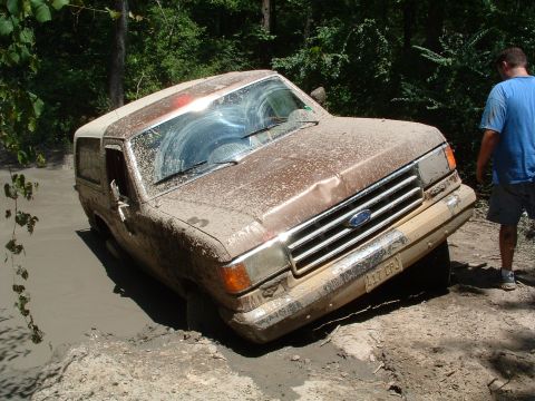 1993 Ford Bronco - A mud-covered 1993 Ford Bronco is stuck in a muddy ditch with a person standing nearby.