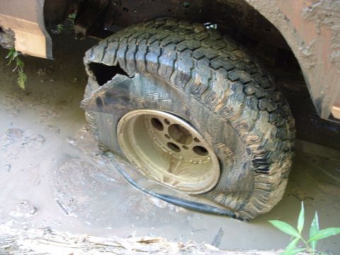 1993 Ford Bronco - A vehicle's tire is severely damaged and stuck in thick mud.