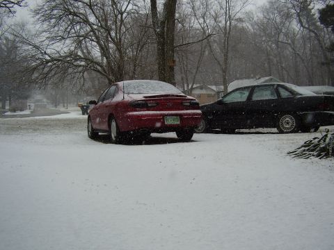 1997 Ford Taurus - Two sedans parked outside during a snowfall, one is a red 1997 Ford Taurus.