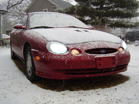 1997 Ford Taurus - A red Ford Taurus sits in the snow, its headlights illuminated.