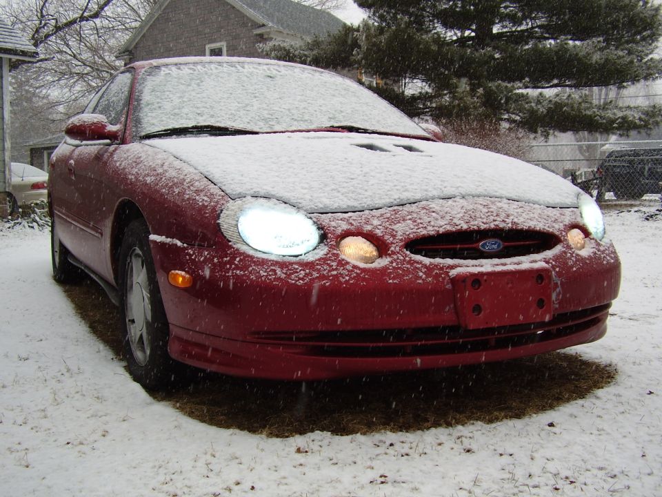 Red Ford Taurus with snow on hood and windshield, front view