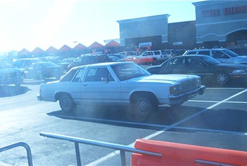 1985 Ford Crown Victoria LTD - A light blue 1985 Ford Crown Victoria LTD is parked in a lot outside a store.