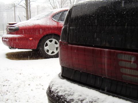1997 Ford Taurus - A red 1997 Ford Taurus sedan is partially covered in snow, viewed from the rear quarter angle.