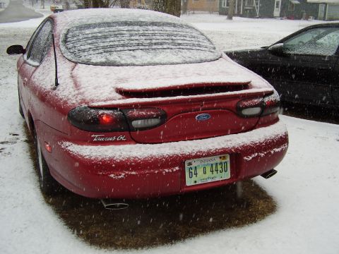 1997 Ford Taurus - Rear view of a red 1997 Ford Taurus GL covered in snow, parked next to another vehicle.