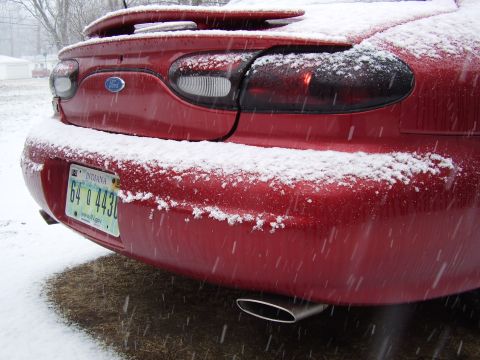 1997 Ford Taurus - A red Ford sedan with snow falling around it, showing its rear end and a license plate.