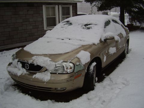 1997 Ford Taurus - A gold sedan, likely a Mercury Sable, sits covered in snow during winter weather conditions that suggest winter weather-related storage.