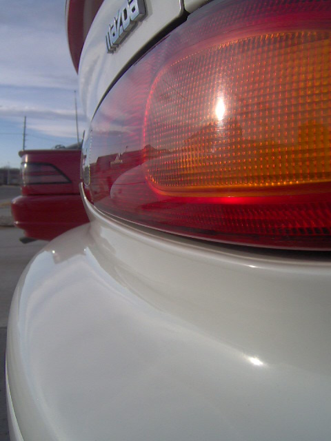 1996 Ford Probe - Close-up of a white Mazda's rear quarter panel and taillight, with another red vehicle visible in the background.