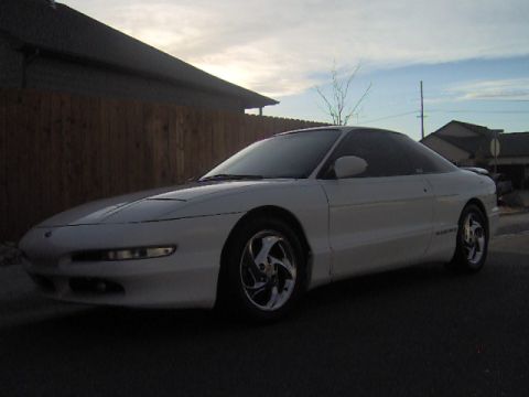 1996 Ford Probe - A white 1996 Ford Probe is parked on a street in front of a wooden fence and a house.