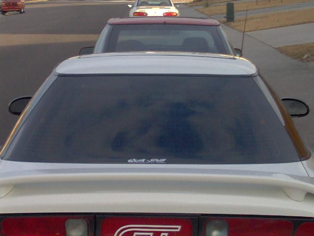 White coupe with a rear spoiler and tinted windows, seen from behind