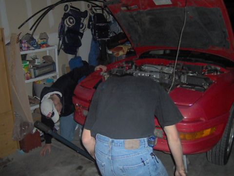1996 Ford Probe - Mechanics work on the engine of a red 1996 Ford Probe in a garage.