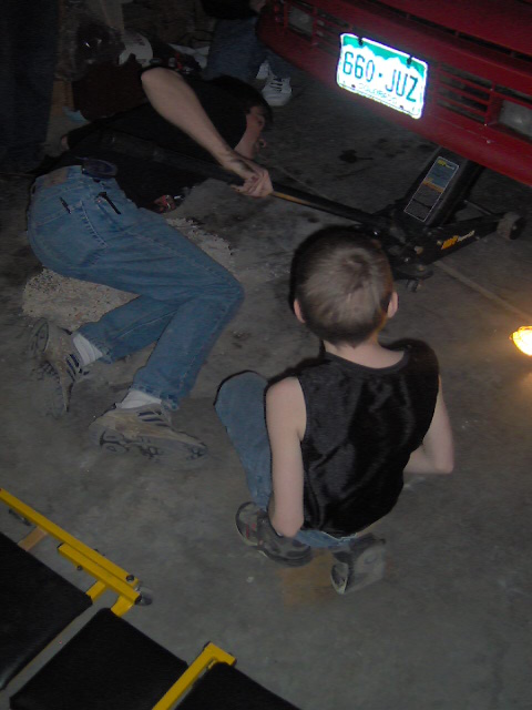 1996 Ford Probe - People are working on a red car being lifted by a jack, with a license plate visible.