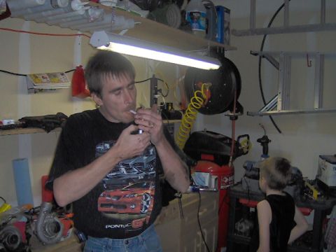1996 Ford Probe - A man smokes a cigarette in a cluttered garage, with a child in the background and a graphic of a Pontiac GTO on his shirt.