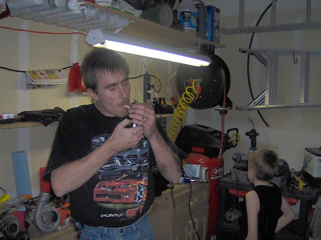 Man smoking in garage, wearing shirt with Pontiac GTO graphic