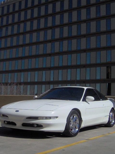 1996 Ford Probe - White 1996 Ford Probe coupe parked in front of a large building with blue-tinted windows.