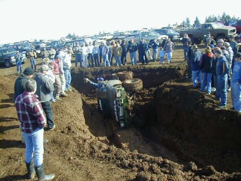 1994 Ford Explorer - An off-road vehicle is stuck on its side in a deep mud pit, surrounded by a crowd of spectators.