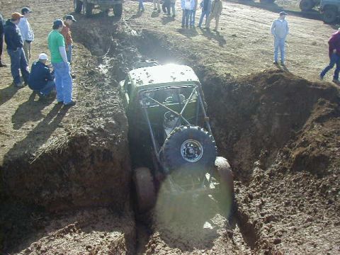 1994 Ford Explorer - An off-road vehicle navigates a challenging mud trench during an event, with onlookers observing the difficult terrain.
