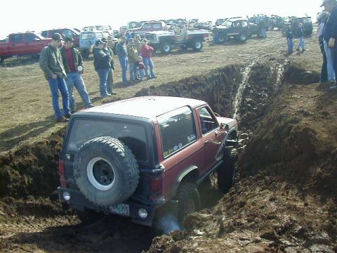 1994 Ford Explorer - A group of people watch as a red SUV navigates a challenging mud pit during an off-road event.