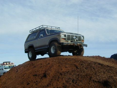 1994 Ford Explorer - This two-tone Ford Bronco, equipped with a roof rack and winch, sits atop a dirt mound during an off-road event.