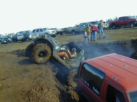 1994 Ford Explorer - An off-road vehicle is stuck in a deep mud pit during an event, with spectators and other vehicles nearby.