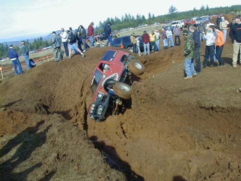 1994 Ford Explorer - A red off-road vehicle is stuck in a muddy trench with spectators watching.