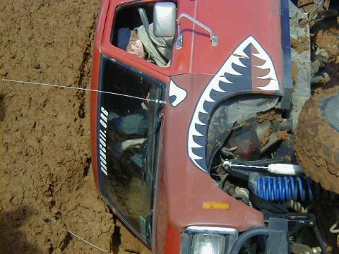 1994 Ford Explorer - A red off-road vehicle with a shark teeth graphic is stuck in thick mud.