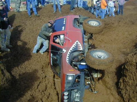 1994 Ford Explorer - A red off-road vehicle is stuck and overturned in a muddy pit during an event.