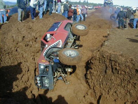 1994 Ford Explorer - A red off-road vehicle is stuck in a deep mud pit, with spectators gathered around.
