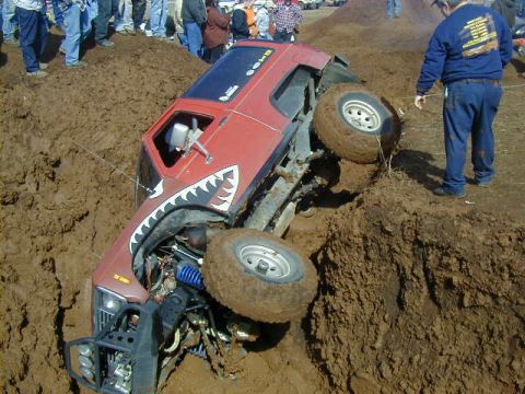 1994 Ford Explorer - A red off-road vehicle is stuck in a muddy pit during an event.