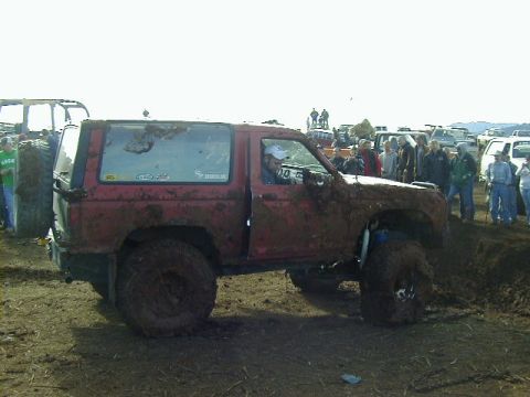 1994 Ford Explorer - A heavily muddied red SUV participates in a mud bogging event, with onlookers gathered around.