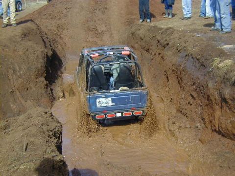 1994 Ford Explorer - A blue off-road vehicle navigates a challenging mud pit during an event.