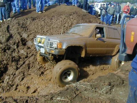 1994 Ford Explorer - A brown SUV navigates a challenging muddy terrain, with spectators watching from a mound.