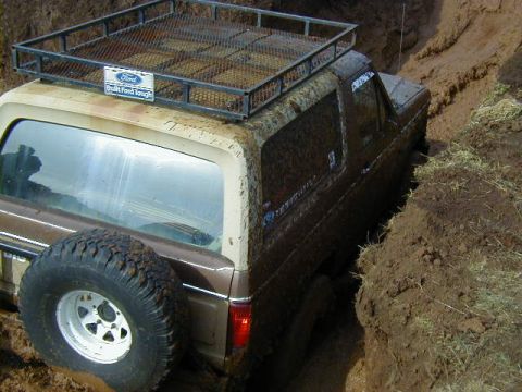 1994 Ford Explorer - A Ford Bronco is deeply stuck in a muddy trench, with only its side visible.