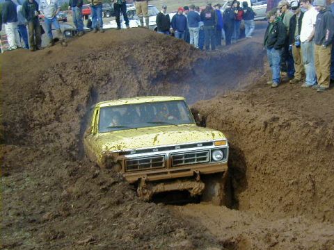 1994 Ford Explorer - A yellow pickup truck navigates a deep mud pit during an event.