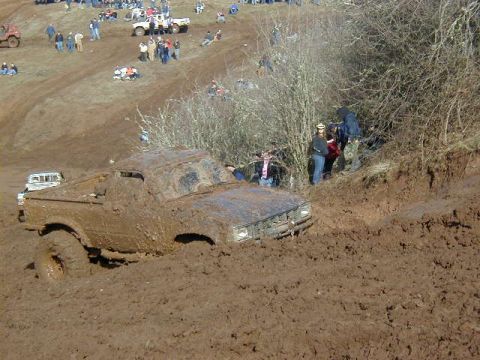 1994 Ford Explorer - A muddy pickup truck struggles in deep mud during an off-road event with spectators in the background.