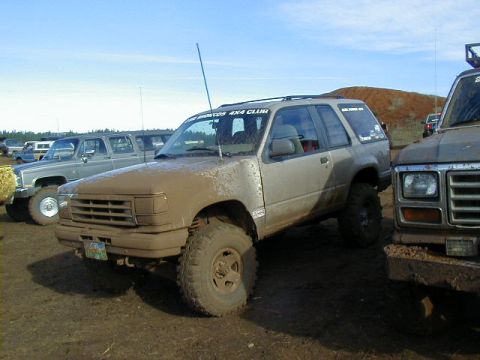 1994 Ford Explorer - Several off-road vehicles are covered in mud at an outdoor event.
