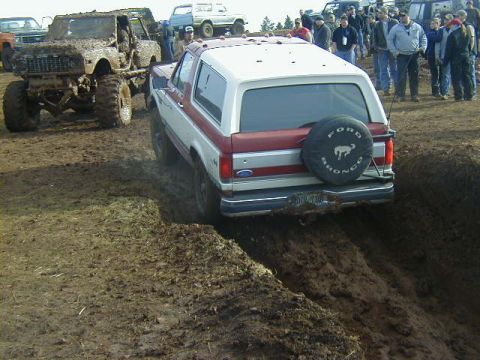 1994 Ford Explorer - A 1994 Ford Bronco navigates a muddy track, with another mud-covered vehicle visible in the background.
