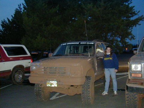 1994 Ford Explorer - A mud-covered SUV is parked next to a woman, with another vehicle visible on the left and right sides.