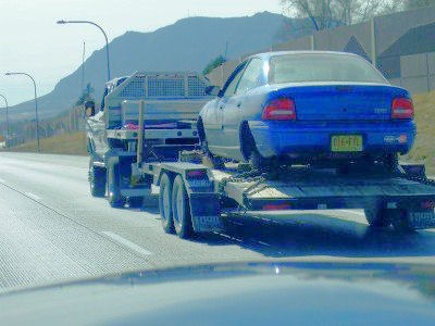 2002 Ford Crown Victoria - A blue sedan is transported on a car hauler trailer on the highway.
