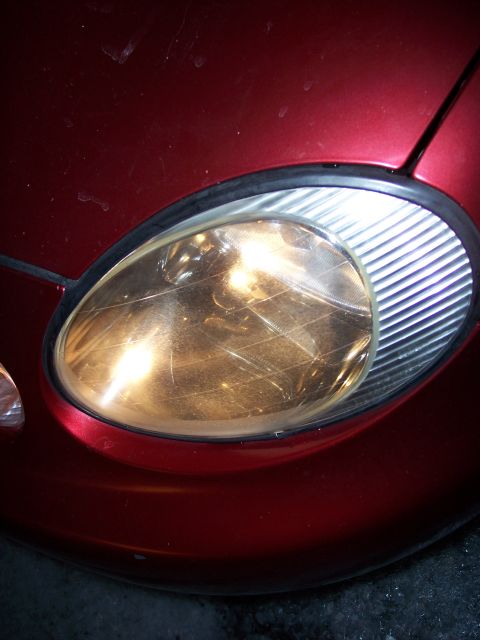 1999 Ford Taurus - Close-up of a scratched headlight on a red vehicle, with "SUPERMOTORS.NET" visible at the bottom right.