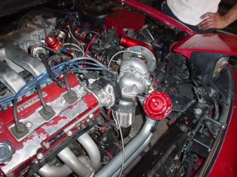 1995 Ford Probe - Close-up view of a modified engine bay a turbocharger and custom exhaust manifold. The red valve cover has 'MAZDA' visible.