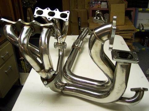 1995 Ford Probe - A shiny chrome exhaust manifold is displayed on a white surface, with shelves and boxes in the background.